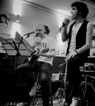 David tocando la guitarra, y Marcos cantando de pie, en un concierto de Conversiones